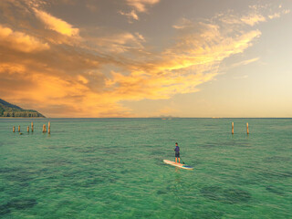 A sunset view with a guy was doing a paddleboard over the beach. 