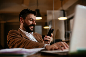 Young businessman using the phone in the office. Handsome man in suit typing a message..