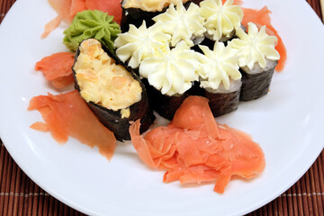 Still-life with appetizing sushi pieces on the white plate on brown wicker straw mat top view close up