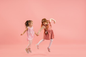 Running. Childhood and dream about big and famous future. Pretty little girls on coral pink studio background. Childhood, dreams, imagination, education, facial expression, emotions concept.