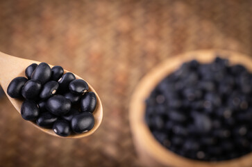 Black beans in a wooden spoon with Black beans in a wooden cup placed on a bamboo weave.