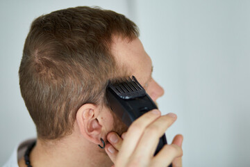 Handsome man in white t-shirts cutting hair personally himself with machine trimmer, clipper at home