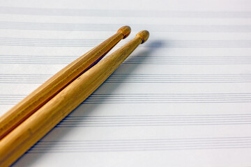 Two wooden drumsticks of light color on a music book on a white table, top view. Hobby music concept, art background, copy space, close-up