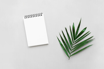 Blank paper notebook with tropical leaf on gray background