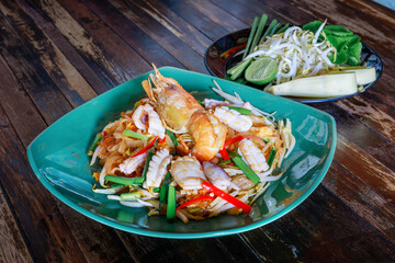 Fried Rice Sticks with Shrimp (Pad Thai Kung Sod) is famous Thai Food dressing with mixed vegetables in white dish placed on wooden background