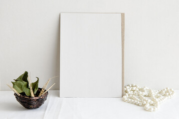 Fashion wedding stationery mockup scene. An empty vertical greeting card and dried white flowers on a white linen background. Feminine still life, top view.