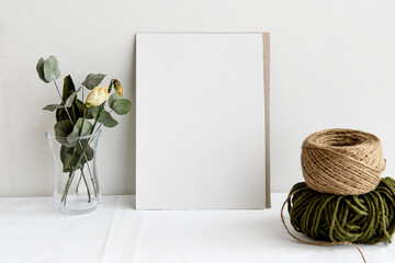 Fashion wedding stationery mockup scene. An empty vertical greeting card and dried white flowers on a white linen background. Feminine still life, top view.