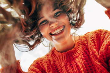 Bottom view of a candid beautiful young woman wearing a knitted orange sweater smiling broadly and...