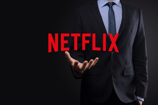 VINOGRADIV, UKRAINE - 04 FEBRUARY 2021. Businessman in a suit on a dark background holds a NETFLIX logo inscription. Google is world's most popular search engine