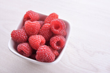 Bowl of fresh raspberries with green leaves on wooden background. Top view