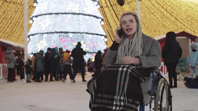 Young woman in a wheelchair at Christmas party on the streets - taking a photo and somebody calls her on the phone