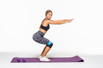 Slim woman doing squats with fitness loop band isolated on white background