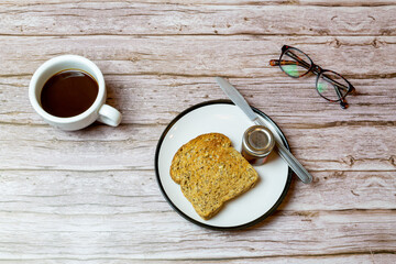 Toast and jam on a plate next to a coffee on a wooden table to represent breakfast time