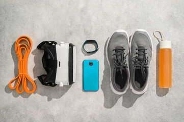 Fitness, workout, and VR technology concept. Sports equipment on grey background: virtual reality glasses, expander, fitness tracker, sneakers, smartphone. Knolling flat lay composition, top view