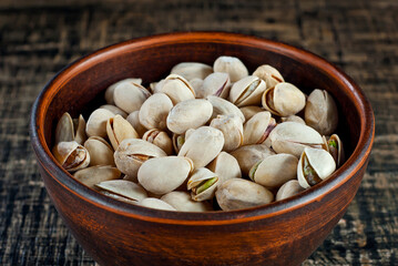 Pistachios in a clay bowl on a shabby wooden board. Nuts in shell on an old black table.