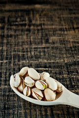 Pistachios in a spoon on a shabby wooden board. Nuts in shell on an old black table. Copy space and free space for text near nuts.