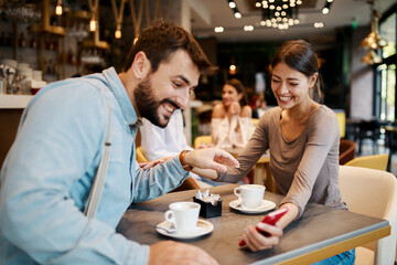 Young happy couple using smartphone in cafe