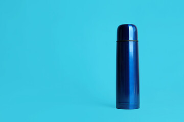 Stylish thermo bottle on light blue background, space for text