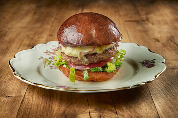 Juicy and appetizing burger with beef, lettuce, mozzarella and tomatoes on a vintage plate on a...