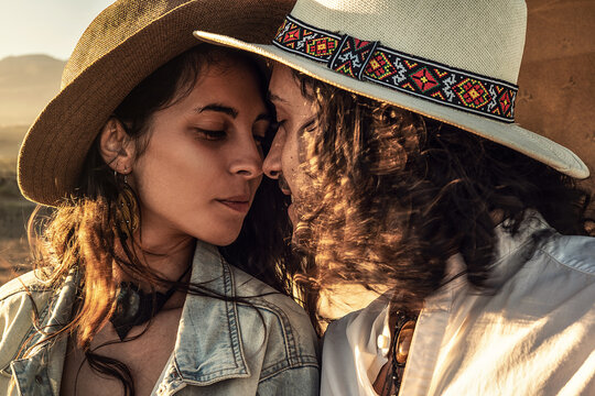 Beautiful couple in love, dating on the beach at sunset, kissing. Fashionable woman and man wearing boho hats. Summer lifestyle. Real people concept.