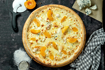 Oven-baked Italian pizza with 4 types of cheese and canned peach in a composition with ingredients on a dark background. View from above