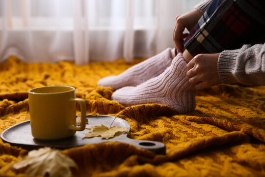 Woman relaxing with cup of hot winter drink on knitted plaid indoors, closeup. Cozy season © New Africa