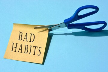 Scissors that cut yellow notepad with bad habits text on a blue background.