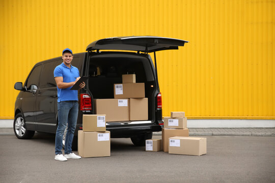 Courier with clipboard and parcels near delivery van outdoors