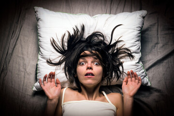 Young girl with a frightened expression wakes up from a nightmare in bed. Woman had a terrible...