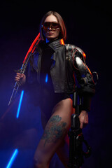 Obraz premium Fantasy portrait of a attractive female soldier with short haircut holding a futuristic sword on her shoulder and gun. Dangerous woman in cyberpunk style going in dark background.