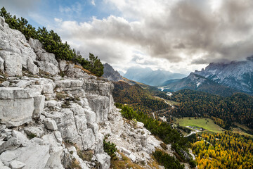 Fototapeta na wymiar Wide angle view of a typical alpine landscape, with a rocky slope on the left and a valley covered by pine trees on the right, under puffy clouds