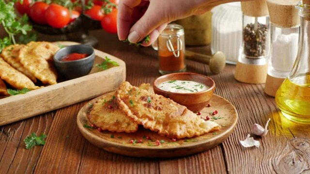Chebureki with sauce. Presentation of the dish. Camera drive along the dish. The cook sprinkles the dish with parsley.