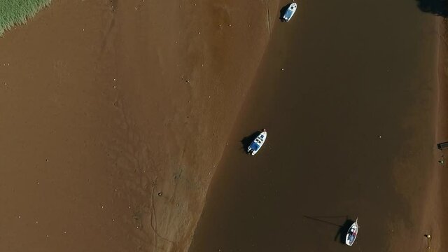Top down of boats moored in a low tide sandy estuary.  Wetland birds scatter the shoreline