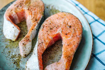 Fresh salmon steaks are marinated in seasonings and in olive oil on a plate
