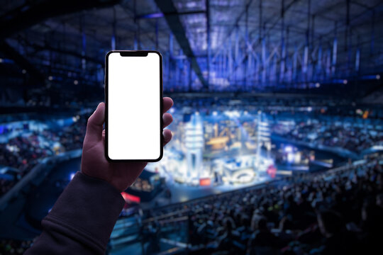 Gamer using smartphone during big esports gaming event sitting on the tribunes inside the arena. Blank screen with copy space mockup