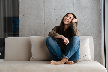 Obraz premium Happy brunette nice girl smiling while sitting on sofa at home