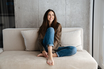Happy brunette nice girl smiling while sitting on sofa at home