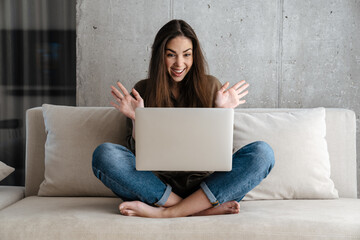 Excited brunette nice girl expressing surprise while using laptop