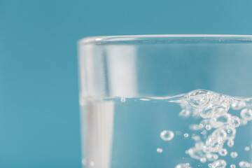 A glass of clear water and bubbles on a blue background close-up.
