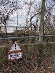 Danger Unsafe Dock Sign On Fence By Old Overgrown River Dock/Pier