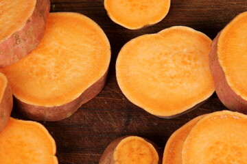 Sliced sweet potato on wooden board background, close up. Raw sweet potatoes or batatas
