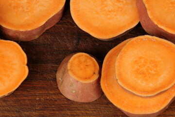Sliced sweet potato on wooden board background, close up. Raw sweet potatoes or batatas