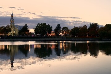 Naklejka premium Catholic Church on the opposite bank of the river, autumn, evening lights, mirroring in the water