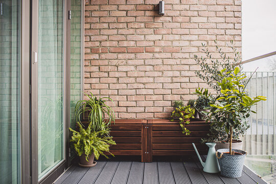 Morden Residential Balcony Garden With Bricks Wall, Wooden Bench And Plants.