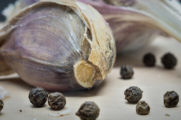 Unpeeled garlic and peas of pepper lie on a wooden board .