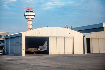 Aircrafts parking inside the hangar in airport and flight control tower behind - obrazy, fototapety, plakaty