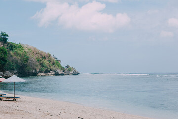 Sea ​​landscape, rocks with trees, white sand beach, and sun loungers. Copy space. Island for relax and chill vacation. 