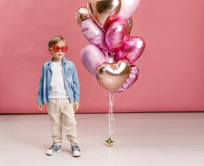 Boy dancing, smiling and having fun near  big branch of pink heart-shaped ballons. Isolated on pink...