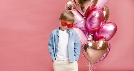 Boy dancing, smiling and having fun near  big branch of pink heart-shaped ballons. Isolated on pink background.