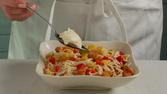 Chinese noodle salad. The cook puts a tablespoon of mayonnaise on the salad. Slow motion. Frontal view.